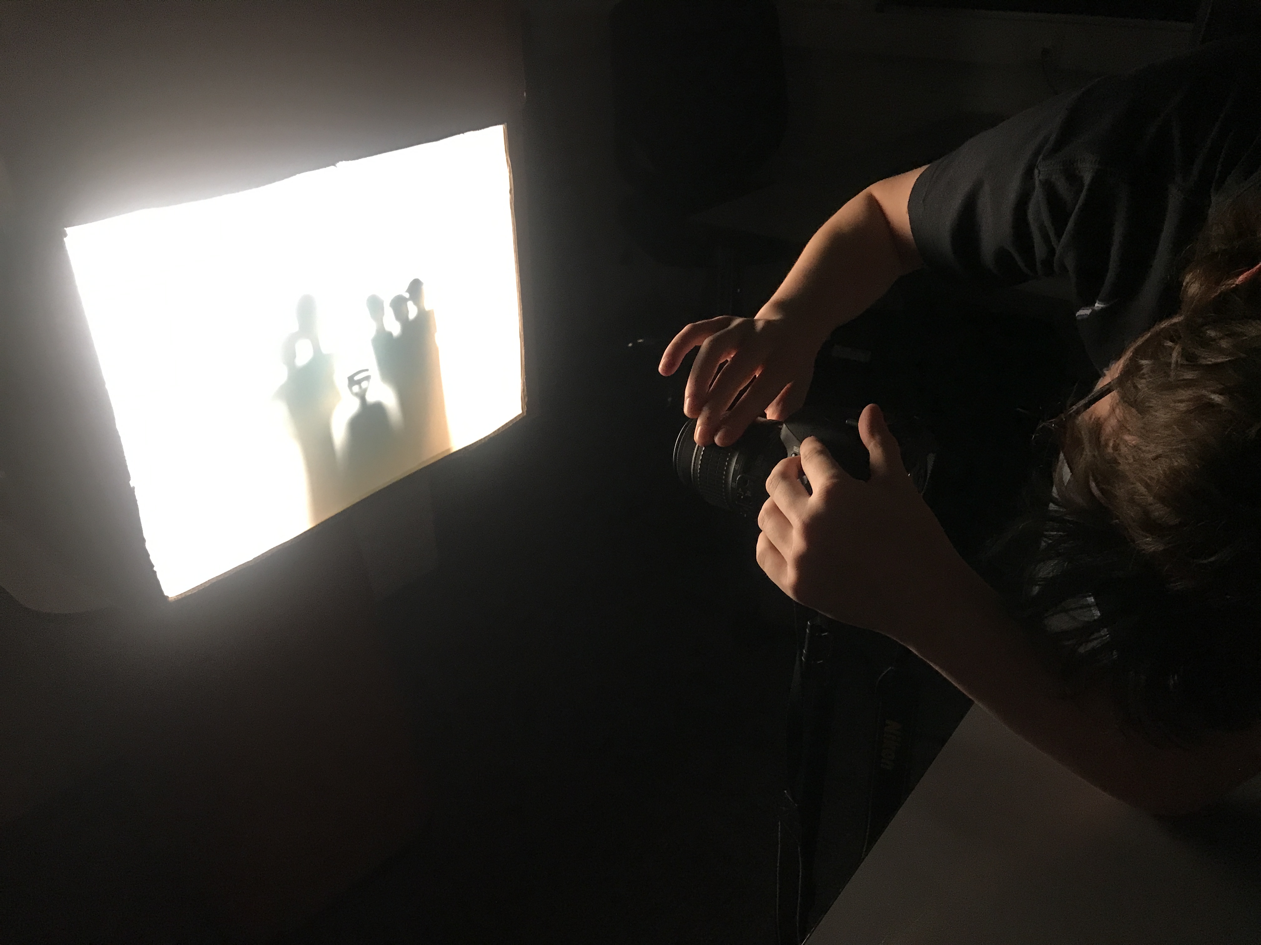 photo of man looking through camera pointed towards shadow box in dark room